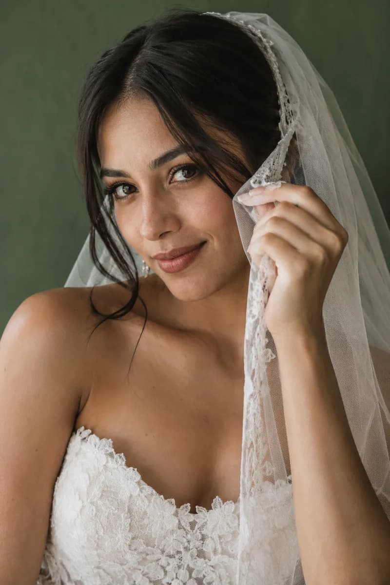 Ilustración creada con IA: novia con cabello liso oscuro sosteniendo el borde del velo cerca de la mejilla