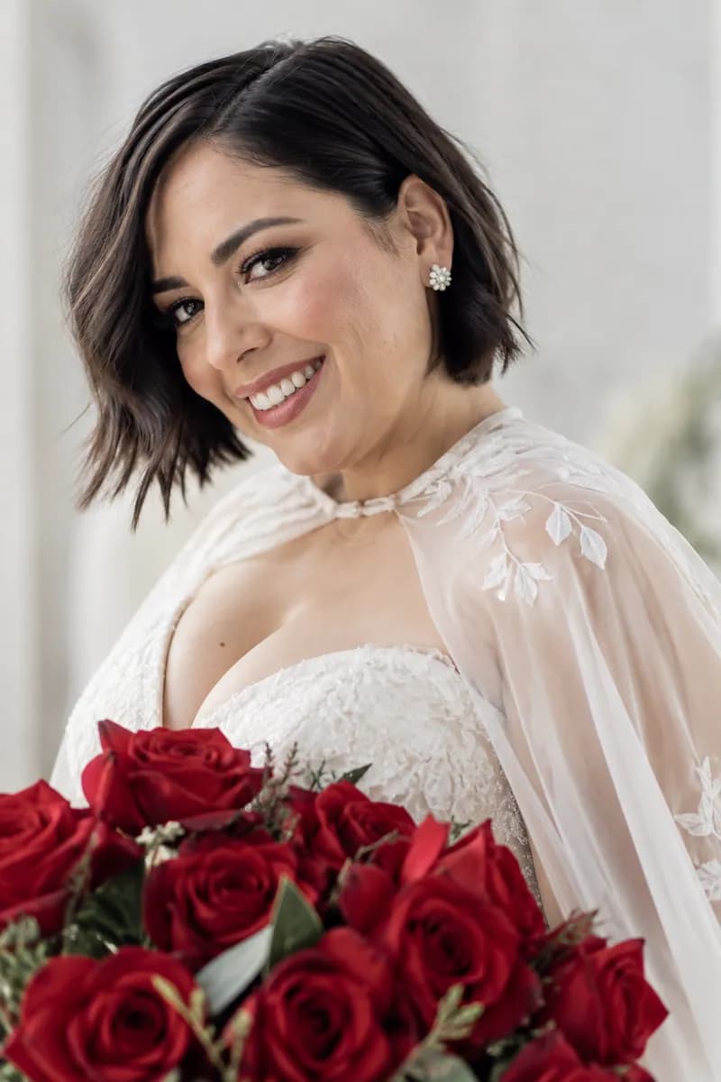 Ilustración creada con IA: novia sonriente con ramo rojo cerca del pecho, cuerpo de tres cuartos y capa transparente