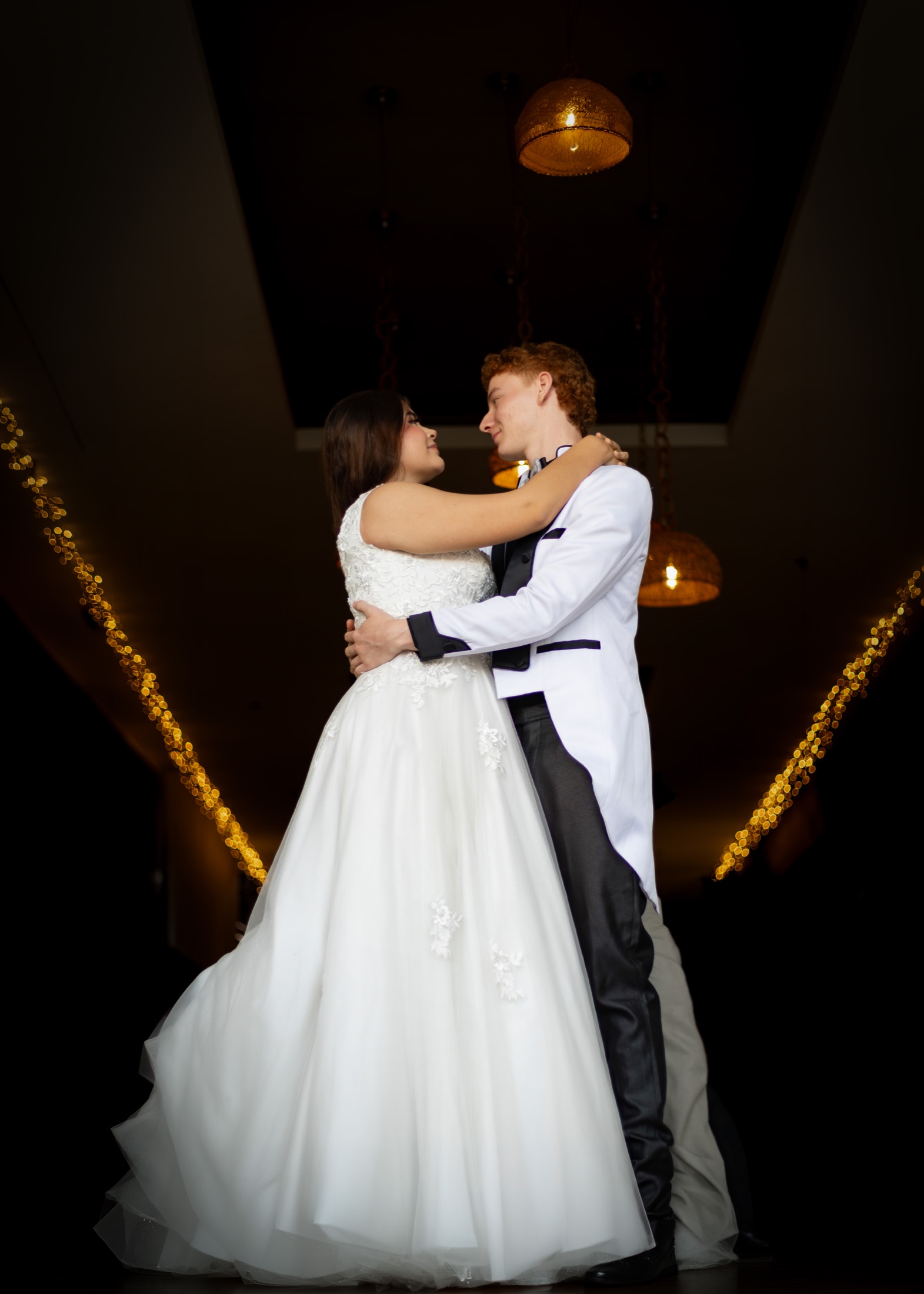 Novios bailando en un salón elegante con luces doradas
