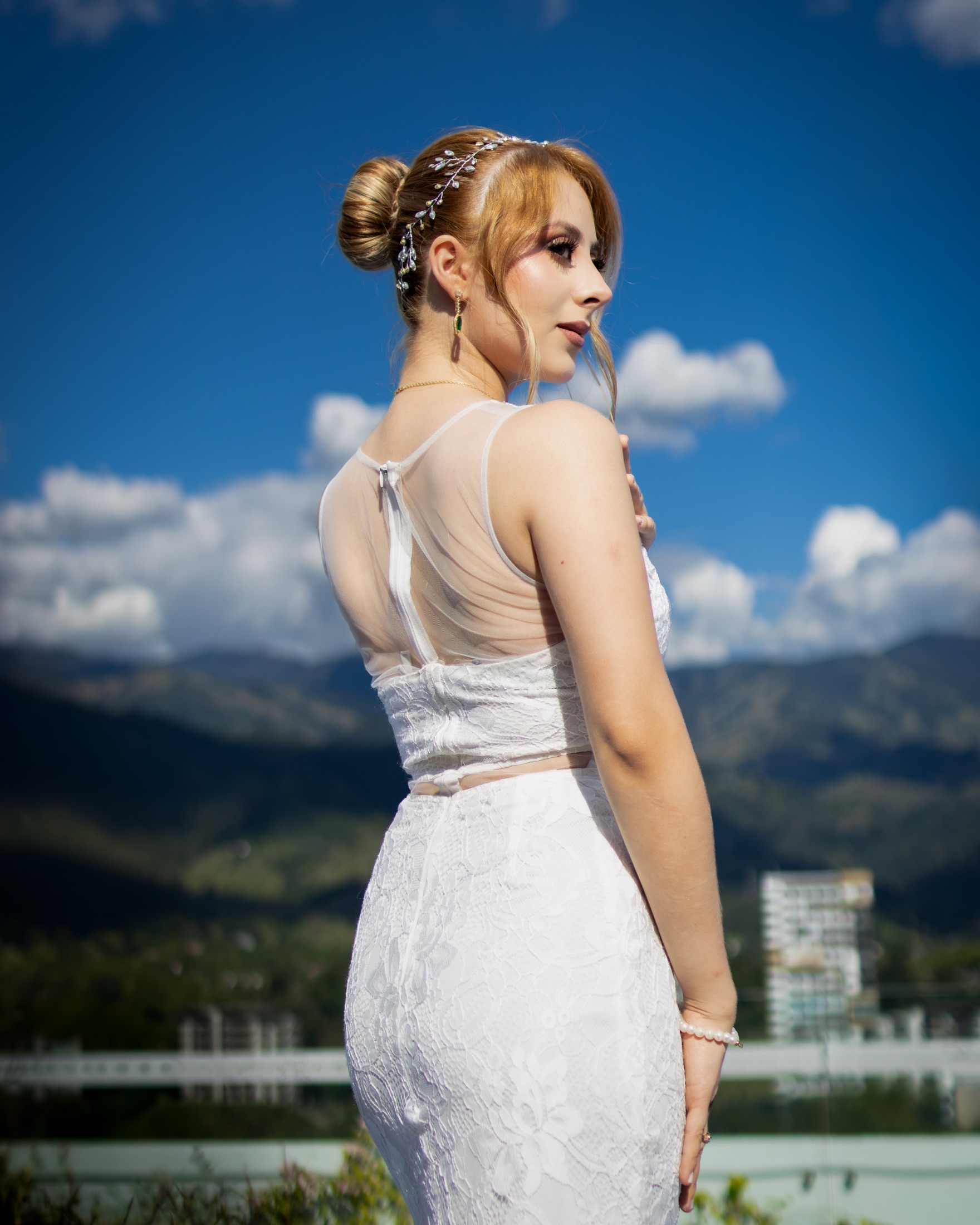 Novia de espaldas contemplando la vista de la ciudad y las montañas