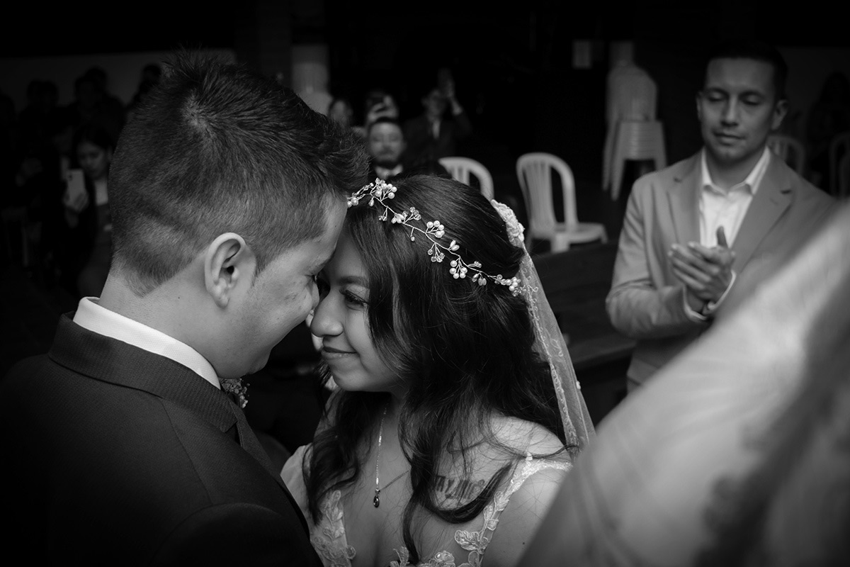 Novios en blanco y negro frente con frente, él con saco oscuro y corbatín