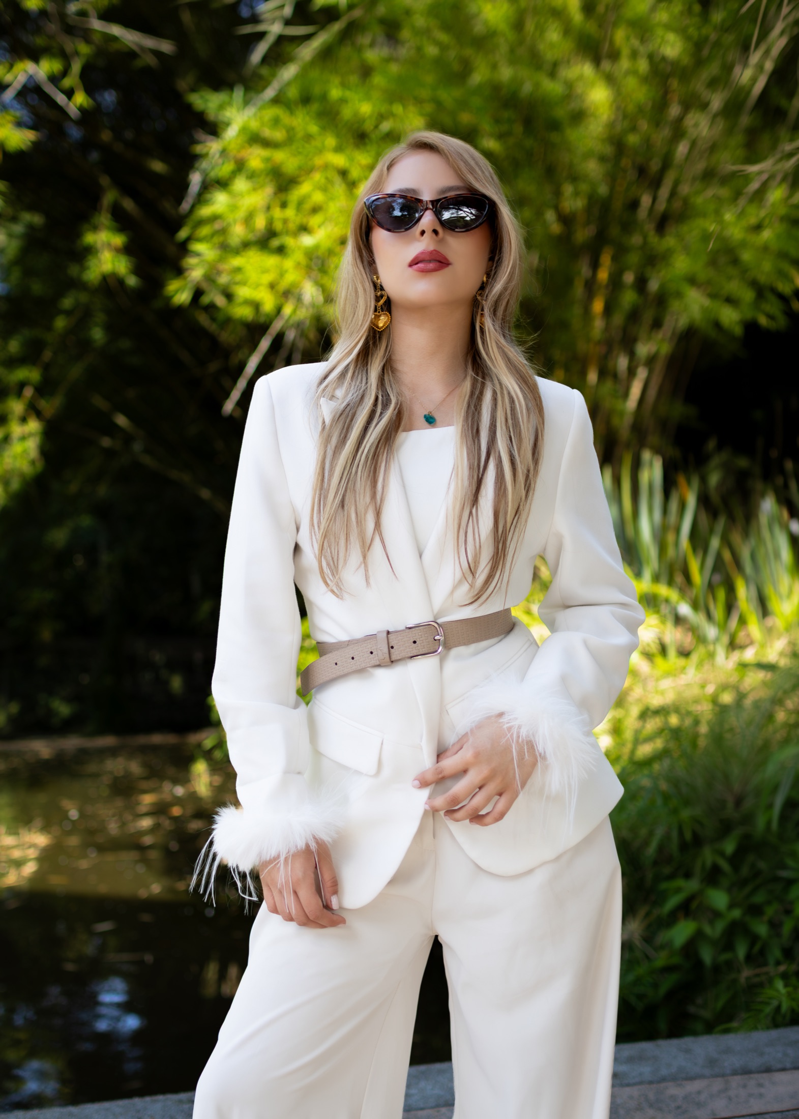 Modelo con traje blanco y gafas de sol posando frente a un jardín de bambú