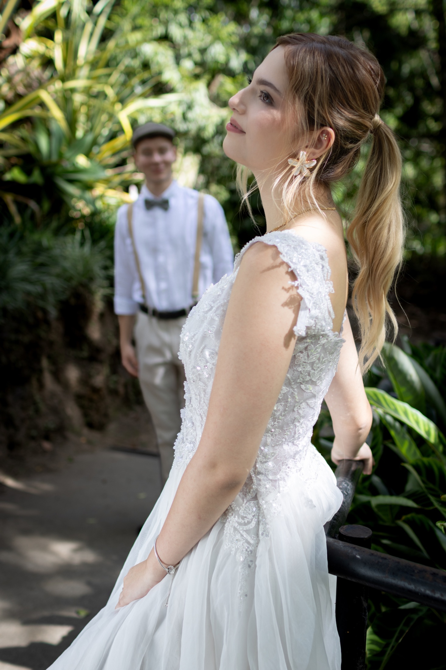Novia de perfil en primer plano con su pareja desenfocada al fondo del jardín