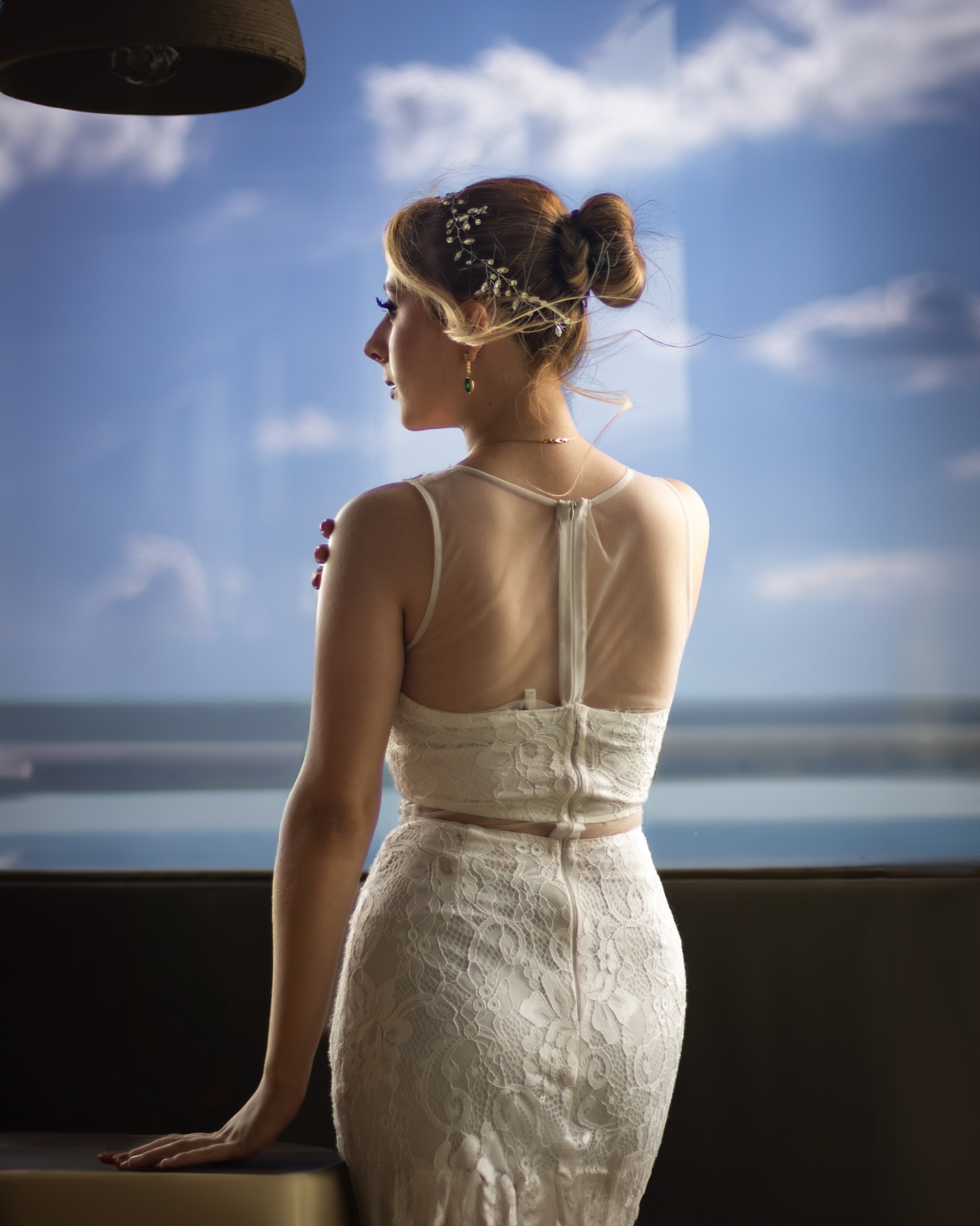 Novia de espaldas contemplando el mar desde una terraza, con un tocado de cristales