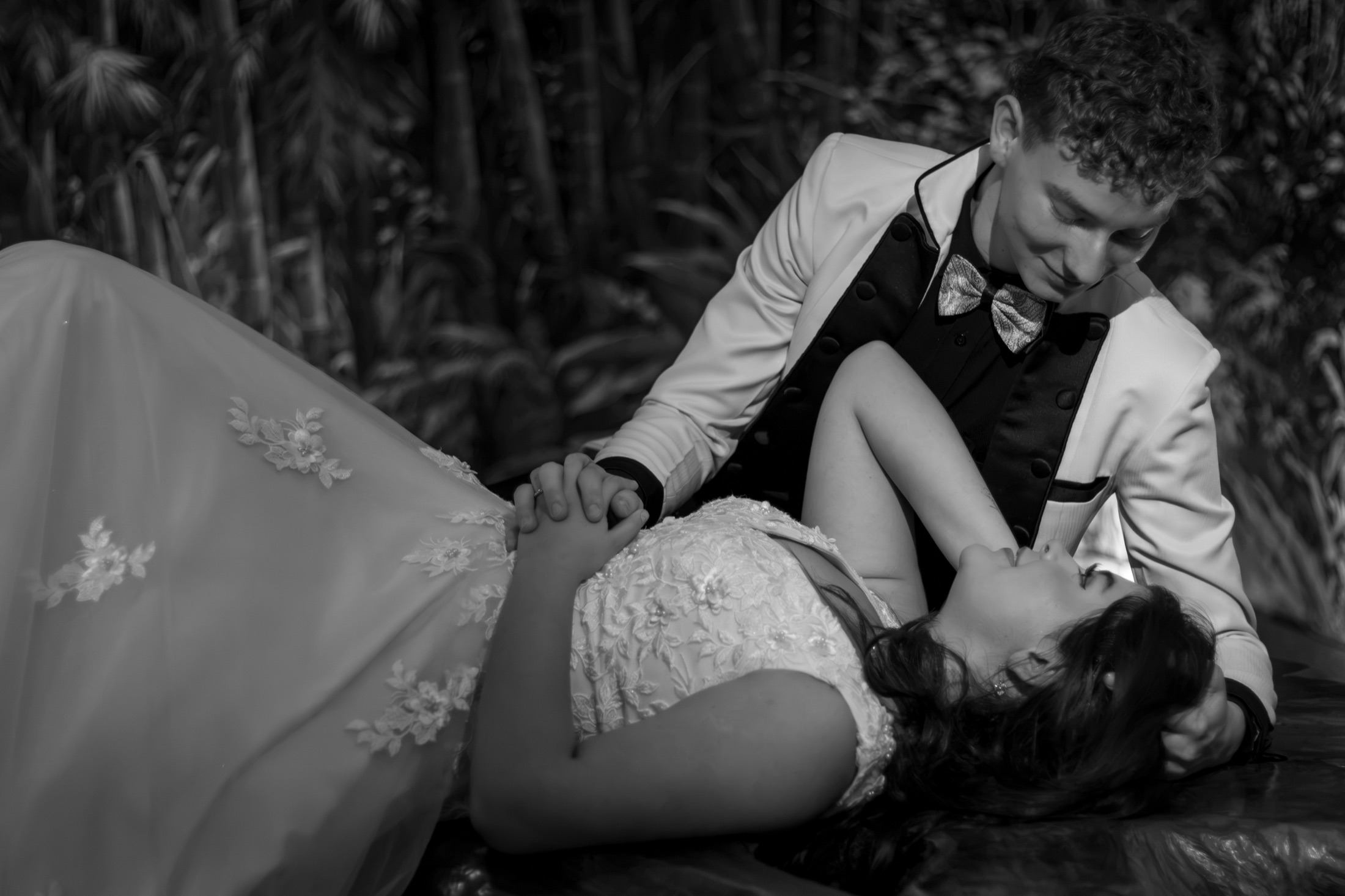 Novios recostados mirándose fijamente entre bambúes, foto en blanco y negro