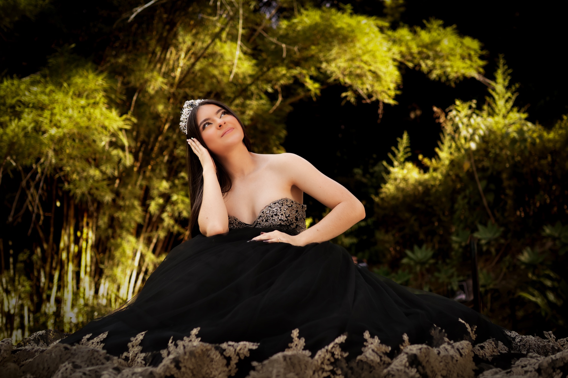 Quinceañera con vestido negro y dorado mirando hacia arriba